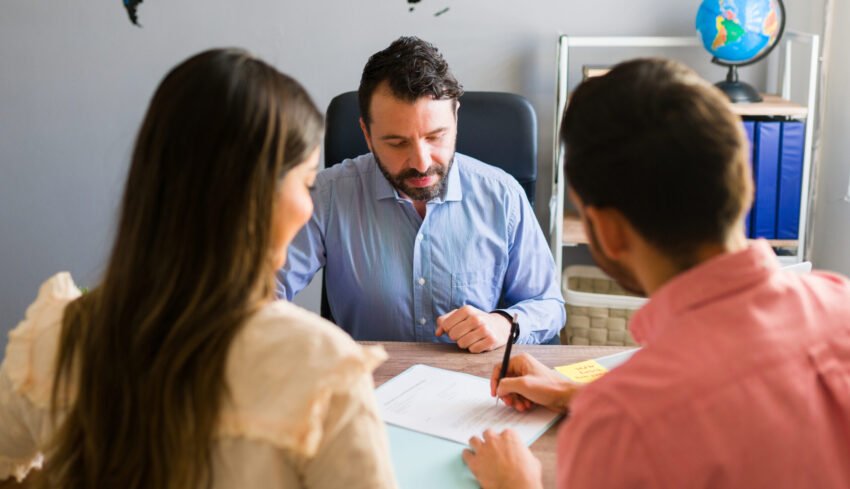 You got a deal. Young man signing a sales contract for a holiday vacation with his wife. Sales representative closing a deal for a timeshare sale with some customers at the travel agency