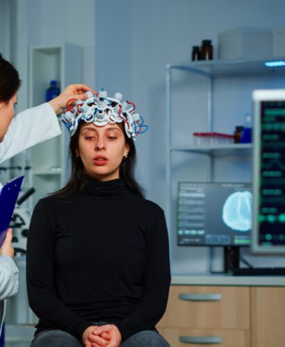 Neurological doctor cheking eeg headset explaining to patient diagnosis of disease and treatment for nervous system. Scientist researcher analysing brain scan and tomography on monitor in lab